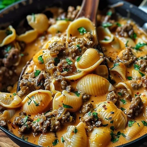 Creamy beef shells casserole topped with cheese and herbs in a baking dish.