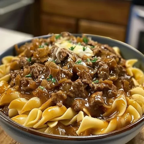 A hearty plate of French onion beef and noodles topped with melted cheese and herbs.