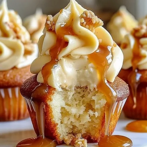 Gooey salted caramel cupcakes with cream cheese frosting on a wooden table.