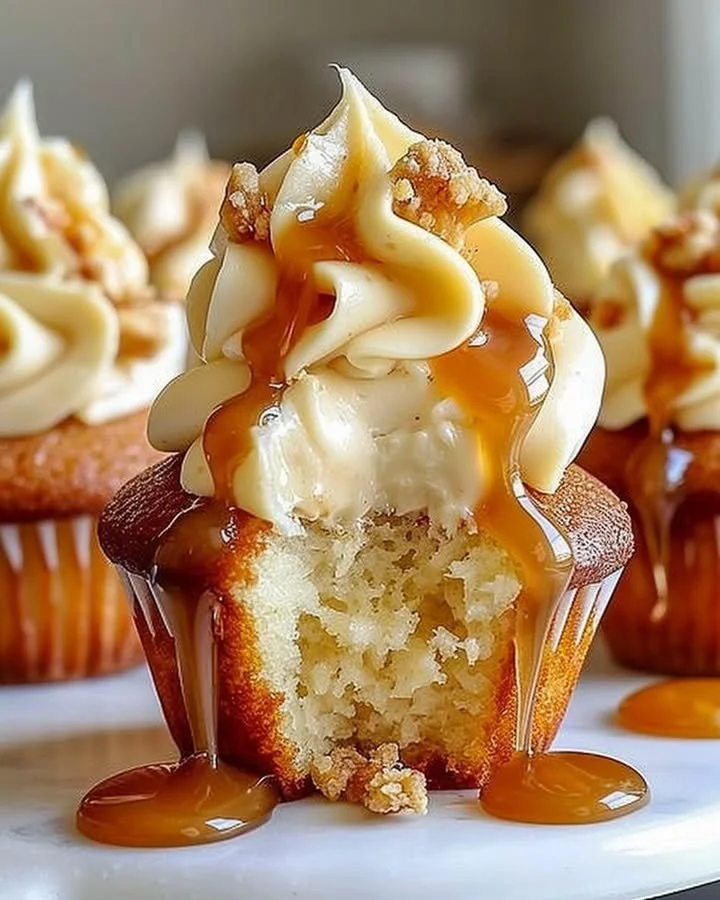 Gooey salted caramel cupcakes with cream cheese frosting on a wooden table.