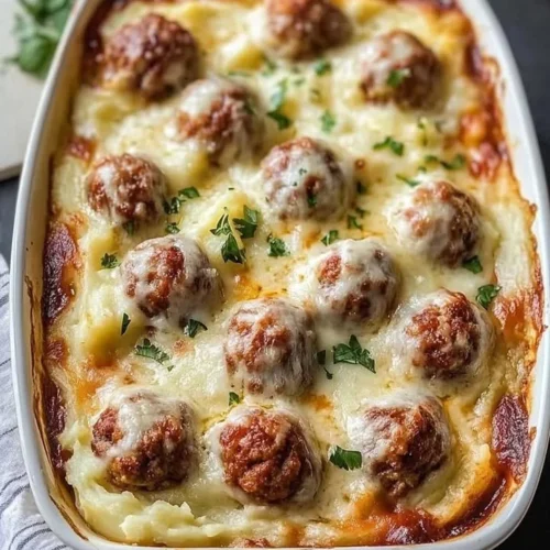 Loaded mashed potatoes casserole topped with meatballs and cheese in a baking dish.