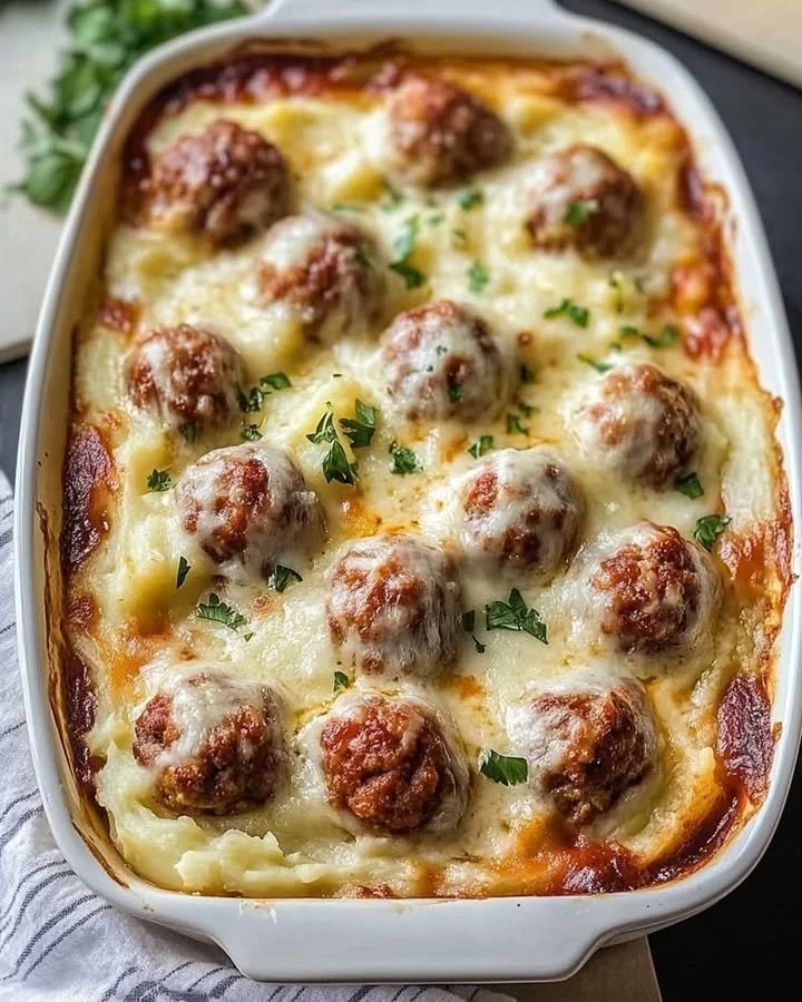 Loaded mashed potatoes casserole topped with meatballs and cheese in a baking dish.